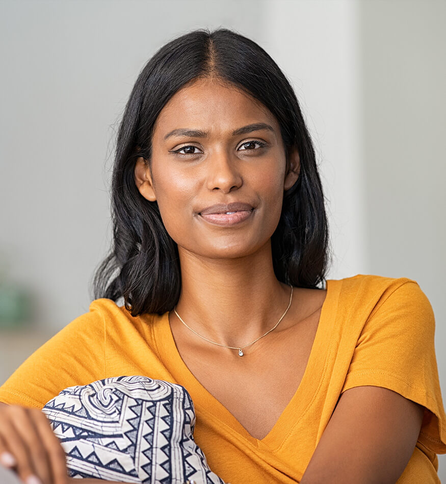 ముఖం మసకబారిన ఒక స్త్రీ ఇంట్లో సోఫాలో కూర్చుని, దిండు పట్టుకుని ఉంది